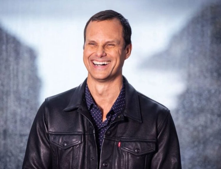 John Needham, Riot Games' President of Publishing & Esports, smiling and wearing a black leather jacket.
